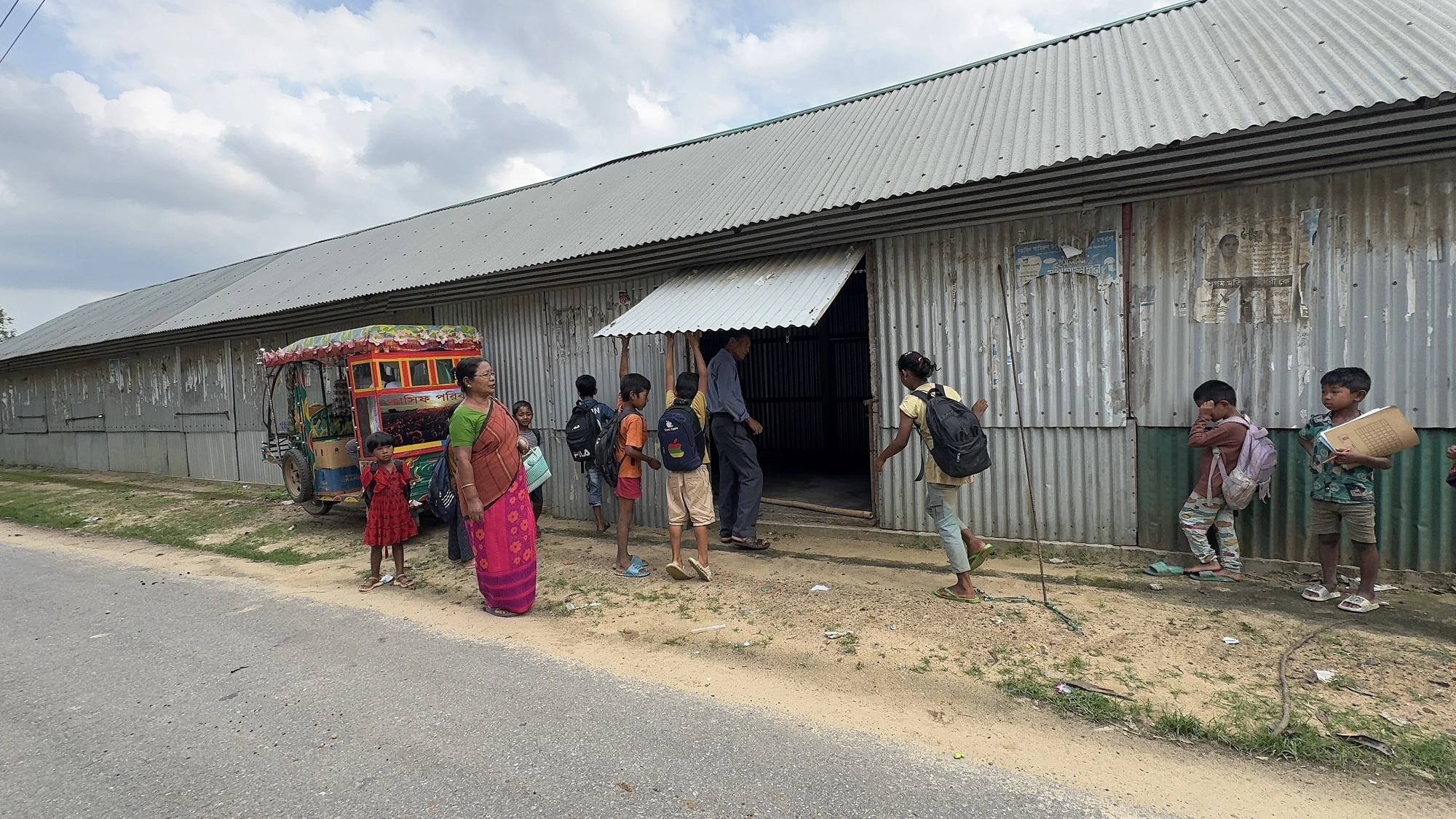 পাঠাশালার দরজা খুলছেন শিক্ষক প্রদীপ ম্রং। শিক্ষিকা লিপি নেংমিঞ্জা শিক্ষার্থীদের পাঠাশালায় প্রবেশের তাগাদা দিচ্ছেন।